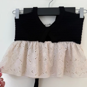 Svart topp från Zara med spets detalj - Supersöt topp från Zara med virkad svart överdel och vit spets i broderad bomull. Perfekt för varma dagar och speciella tillfällen. Snörena kan man knyta runt nacken så blir det en öppen rygg.