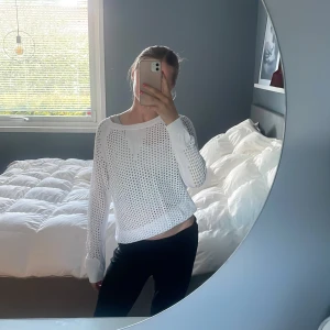 Vit stickad croppad tröja - Säljer en vit stickad croppad tröja med hålmönster och långa ärmar. Tröjan har en avslappnad passform och är perfekt för lager-på-lager. Snygg till både jeans och kjol!
