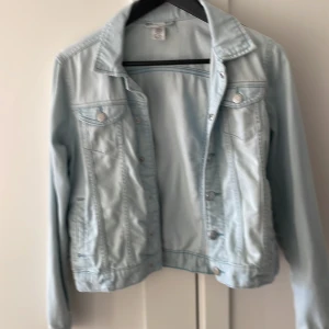 Ljusblå jeansjacka från Lindex - Säljer en klassisk ljusblå jeansjacka från Lindex. Jackan har knappar framtill, två bröstfickor med lock och knapp samt klassisk krage. Perfekt att slänga över en t-shirt för en avslappnad look.
