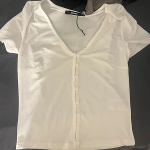 Vit kortärmad blus från bikbok - Säljer en vit blus från Bikbok med korta ärmar och v-ringning. Blusen har knappar framtill och är tillverkad i ett lätt material. Aldrig använd