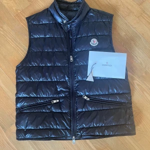 Moncler gui väst - En Moncler gui väst i marinblå färg. Storlek 2 ~ S/M. 2022 modell och i grymt skick utan flaws. Medföljer tomt Moncler kuvert och triangel. Äktehetsbevis visas på bild. 