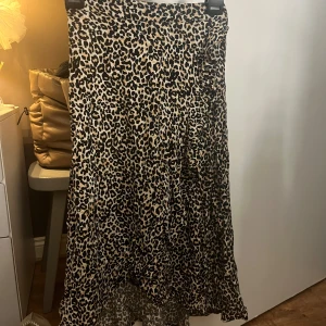 Leopardmönstrad lång-kjol från Lindex - Säljer en snygg leopardmönstrad lång-kjol från Lindex med asymmetrisk nederkant. Kjolen har elastisk midja och är i mjukt, lätt tyg som ger ett fint fall. Perfekt för dig som hänger på trenden leopard och vill sticka ut lite extra. 