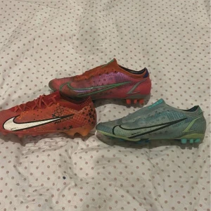 Nike Mercurial fotbollsskor i olika färger - Tre par Nike Mercurial fotbollsskor i rött, rosa och ljusblått. Skorna har snörning, låg profil och platt sula med dobbar för bra grepp på planen. Perfekta för dig som vill sticka ut på fotbollsplanen. 500 kronor för varje par