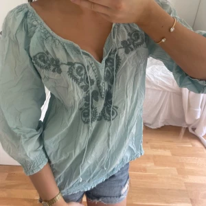 Blus med broderi - Säljer en ljusblå blus med v-ringning och mörkare blått broderi framtill. Perfekt till sommaren! Står storlek 42 men passar mig som brukar ha S i toppar🤗