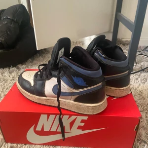 Nike Air Jordan 1 Mid svart/blå/vit - Säljer ett par Nike Air Jordan 1 Mid i svart, blått och vitt Äkta. Skorna har klassisk hög siluett, svart snörning och blåa detaljer på sidan och tungan. Perfekta för dig som gillar streetwear och sneakers med ikonisk design.