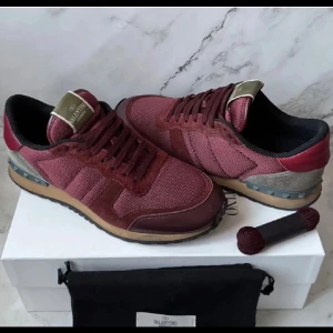 I✨Valentino Rockrunner sneakers i vinrött och grått✨ - Säljer ett par Valentino Rockrunner sneakers i vinrött med detaljer i grått, beige och rött. Skorna har snörning, rund tå och platt sula. Klassisk design med mix av mocka och skinn samt ikoniska nitar på sulan. Och självklart är dom autentiska ✨