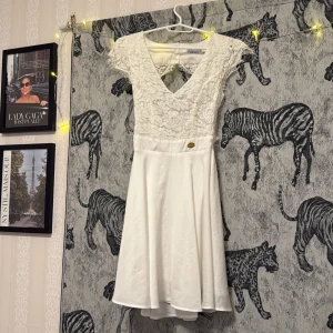 Vit studentklänning från Chiara Forthi - Söt vit klänning från Chiara Forthi med spets upptill, v-ringning och öppen rygg. Kjolen är lätt utsvängd och klänningen har en liten guldfärgad detalj i midjan. Perfekt för student/skolavslutning. Har haft denna på skolavslutningen/studenten och fick så många komplimanger<3