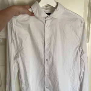 Vit skjorta med klassisk krage - Säljer en stilren vit skjorta med klassisk krage och knäppning framtill. Skjortan har långa ärmar och är perfekt för dig som vill ha en clean och enkel look. Passar till många olika outfits
