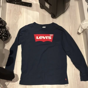 Mörkblå långärmad tröja från Levi's - Säljer en mörkblå långärmad tröja från Levi's med den klassiska röda loggan framtill. Tröjan har rund halsringning och är i mjuk bomull, perfekt för en avslappnad stil.