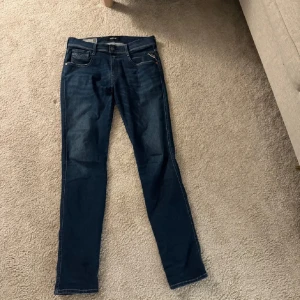 Mörkblå Replay Anbass jeans - Säljer ett par mörkblå Replay Anbass jeans med klassisk femficksdesign och snygga kontrastsömmar. Jeansen har normal passform och raka ben, perfekt för dig som gillar stilrena och tidlösa jeans. Märkeslapp bak i midjan.