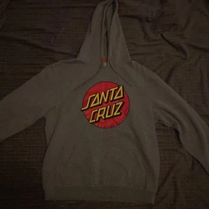 Grå hoodie från Santa Cruz - Säljer en grå hoodie från Santa Cruz. Tröjan har en klassisk känguruficka. 
