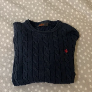 Mörkblå stickad tröja från Morris - Säljer en snygg mörkblå stickad tröja från Morris med storlek XS med ett flätat mönster. Tröjan har en liten röd logga på bröstet och långa ärmar. Säljer den för 660kr ett väldigt bra pris när nypris är 1799 är alltid öppen för prisförslag. Perfekt för kyligare dagar! Köpare betalar frakt