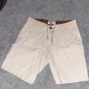 Linne shorts - Snygga beige shorts med snörning i midjan och knappdetaljer. Perfekta för en avslappnad stil. De har två fickor fram och två bakfickor med knappar. Kommer se nya ut när man stryker