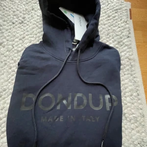 Dondup hoodie  - Säljer en stilren mörkblå hoodie från Dondup med texten 'MADE IN ITALY' tryckt på framsidan. Tröjan har en klassisk design med huva och dragsko samt en stor ficka framtill. Perfekt för en avslappnad look. Storleken är L. Alla tags finnskvar och produkten är aldrig använd 