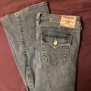 Blå jeans från True Religion - Säljer ett par snygga och bekväma True Religion- jeans i låg midja. De har en bootcut-stil och är mer ljus blåa i verkligheten (kolla sista slide). Tyvärr är de för stora på mig så säljer just nu dem vidare!! Skicket är helt nya, då jag har endast provat dem!! Storlek: W 29. Inköp pris: 1299 kr