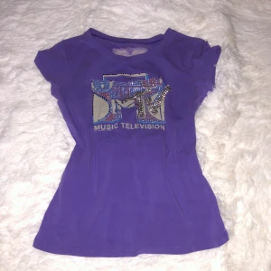 Lila MTV t-shirt med paljetter - Säljer en snygg lila t-shirt med ett glittrigt MTV-tryck på framsidan. Väldigt retro så många stenar är tyvärr av men jag tycker inte att det gör nått 😋men hade säkert varit kul att pyssla med att sätta dit egna stenar! Står ingen storlek men skulle gissa på S/liten M