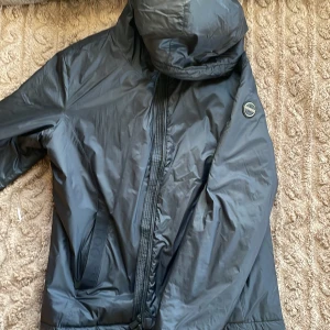 Svart vindjacka från Snoot Stockholm - Snygg svart vindjacka från Snoot Stockholm i storlek XL. Jackan har en dragkedja framtill och en praktisk huva. Perfekt för blåsiga dagar och har en stilren design med en liten logotyp på ärmen. Jag har storlek M i jackor men denna passar mig. 