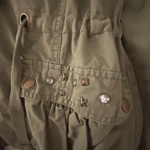 Grön jacka med snygga detaljer - Skitcool grön jacka med fickor och band i mindjan som man kan dra åt om man vill. På ena ficka lite nitar, stjärnor och stenar! Skitsnygg men tyvärr lite lite på mig därför så dåliga bilder!!🤗🤗🤗 