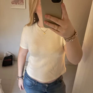 Vit kortärmad topp - Säljer en stilren krämvit topp. Toppen har en rund halsringning och är i ett mjukt material.