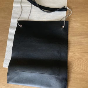 Svart Fillipa K axelväska med silverdetaljer - Snygg svart axelväska i skinn med stilrena silverdetaljer. Väskan har en enkel design med en praktisk axelrem och en rymlig insida. Perfekt för att bära med sig det nödvändigaste med stil.