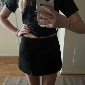 Svart minikjol - Svart kort kjol från Zara. Helt oanvänd med lappen kvar på! Har inbyggda shorts och en slits detalj på sedan, även dragkedja på kanten. Passar till så många outfits. Storlek xs. Skriv ifall fler frågor/bilder💞