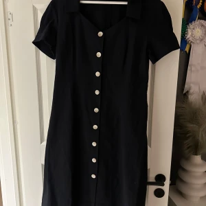 Helt ny svart klänning  - Säljer denna svarta klänning med fina vit/beiga knappar. Helt ny, aldrig använd, prislappen kvar❤️
