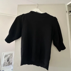 Svart stickad t-shirt från Jdy - Säljer en svart stickad tröja med trekvartsärmar och ribbad hals. Perfekt för kyligare dagar och enkel att matcha med olika outfits.