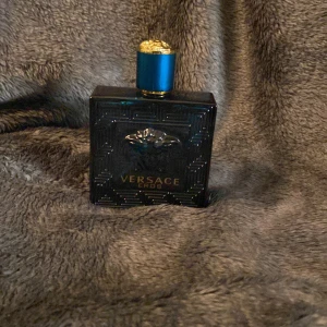 Versace Eros Eau de Toilette 100 ml - Säljer en flaska Versace Eros Eau de Toilette, ungefär 95-90 ml kvar . Flaskan är i en elegant blå färg med ett gyllene lock prytt med Versaces ikoniska Medusa-motiv. Doften är känd för sina friska och maskulina noter, perfekt för den självsäkra mannen.
