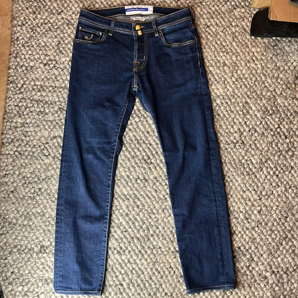 Snygga blå jeans från Jacob Cohen med en slim passform. De har klassiska fem fickor och en knappgylf. Märkeslogga på baksidan och kontrastsömmar som ger en stilren look.. Farkut & Housut.