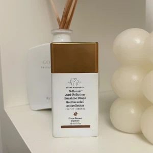 Drunk Elephant D-Bronzi Anti-Pollution Sunshine Drops - Drunk Elephant D-Bronzi Anti-Pollution Sunshine Drops i en stilren flaska med bronsfärgat lock. Innehåller kakaoutdrag och peptider för att ge en solkysst look och skydda mot föroreningar. Perfekt för att blanda med din dagkräm eller foundation för extra lyster. Uppskattar att det är lite mer än hälften kvar i den.