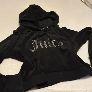Säljer en snygg svart hoodie från Juicy Couture med glittrande stenar som bildar texten 'Juicy' på framsidan. Hoodien har en klassisk design med huva och dragsko. Perfekt för en avslappnad och stilren look.