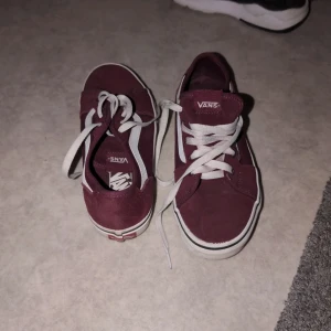 Vinröda sneakers från Vans - Säljer ett par snygga vinröda Vans sneakers med vit sula och klassisk snörning. Perfekta för en avslappnad stil och bekväma att bära hela dagen. De har en tidlös design som passar till det mesta.