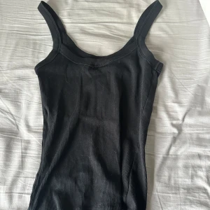 Svart ribbad linnetopp från Gina Tricot - Snygg svart ribbad linnetopp från Gina Tricot. Perfekt för lager-på-lager eller att bära som den är. Den har breda axelband och en klassisk design som passar till allt. Ett måste i garderoben!