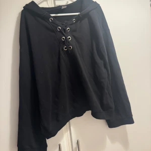 Svart hoodie med snörning - Säljer en svart hoodie med cool snörning framtill. Långa ärmar. Huvan ger extra mysfaktor. Perfekt för höst och vinter!