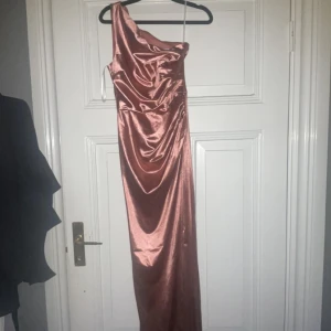 Rostfärgad sidenklänning - Elegant rostfärgad långklänning i siden med en stilren oneshoulder-design. Perfekt för en glamorös kväll med sin glänsande yta och smickrande passform.