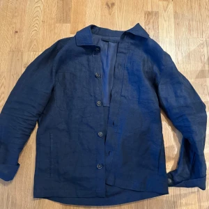 Mörkblå linnéovershirt med knappar - Säljer en stilren mörkblå overshirt i linne med knäppning framtill. Jackan har klassisk krage, raka ärmar och två diskreta fickor framtill. Perfekt för lager-på-lager och ger en avslappnad men snygg look. Märket är mango och storleken är S men sitter som en S/M och om du har några funderingar är det bara att höra av sig:)