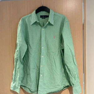 Grön rutig skjorta från Ralph Lauren - Säljer en grön och vit rutig skjorta från Ralph Lauren i slim fit-modell. Skjortan har långa ärmar, klassisk krage och knäppning framtill. Den har en rosa broderad logga på bröstet och är perfekt för dig som gillar stilrena detaljer.
