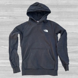 The North Face Hoodie - Säljer en svart hoodie från The North Face med vit logga på bröstet och stor logga med texten 'Never Stop Exploring' på ryggen. Tröjan har huva, magficka och ribbade muddar vid ärmslut och nederkant.