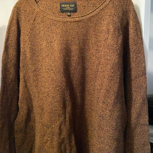 Brunmelerad stickad tröja från Denim Day - Säljer en brunmelerad stickad tröja från Denim Day. Tröjan har rund halsringning och långa ärmar. Perfekt för kyligare dagar och enkel att matcha med olika outfits.
