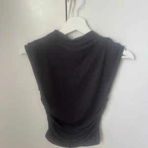 Grå ärmlös topp från Gina Tricot - Säljer en grå/blå ärmlös topp från Gina Tricot. Toppen har en tight passform och är lätt rynkad i sidorna för en snygg siluett. Perfekt att matcha med jeans eller kjol för en trendig look.