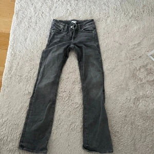 Grå jeansbyxor med raka ben - Säljer ett par grå jeansbyxor med raka ben och klassisk femficksdesign. Byxorna har bälteshällor och knäppning fram. Perfekta för dig som gillar en enkel och stilren look.