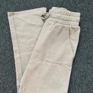 Beige mjukisbyxor med resår och snörning - Beiga mjukisbyxor från 157 med resår i midjan och snörning. Byxorna har två sidofickor fram och en bakficka. Perfekta för en avslappnad stil och tillverkade i mjukt bomullsmaterial.