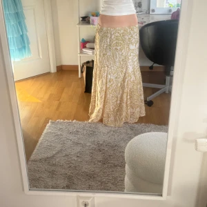 Gul och vit långkjol med bladmönster - Säljer en flowy långkjol i gul och vitt med ett snyggt bladmönster. Kjolen har en lös passform och är perfekt för varma dagar. Resår i midjan för extra komfort.