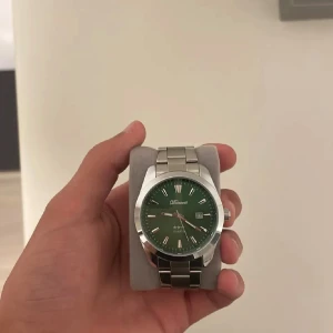 Grön herrklocka från Doventi med metallarmband - Stilren klocka från Doventi med grön urtavla, silverfärgat boett och länkarmband i metall. Klockan har datumvisning och romerska siffror på urtavlan. Perfekt accessoar för dig som gillar klassisk design.