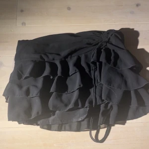 Mini skirt  - Säljer en svart kortkjol från SHEIN med flera lager volanger och knytband i midjan. Kjolen har en feminin och trendig look som passar perfekt till olika outfits. Materialet känns lätt och flowy.  Funkar som topp