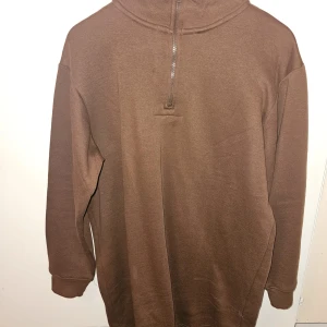 Brun halvzip-tröja från Threadbare - Säljer en brun långärmad tröja från Threadbare med halv dragkedja framtill och hög krage. Tröjan har ribbade muddar vid ärmslut och är i mjukt material, perfekt för kyligare dagar.