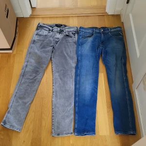 Två par Replay jeans, grå och blå, w30 l30 - Säljer två par Replay jeans i storlek w30 l30. Ena paret är gråa och det andra är klassiskt blå. Båda har raka ben, fem fickor och normal passform. Perfekta för dig som gillar stilrena och tidlösa jeans. (Dom grå jeansen har tyvärr gått sönder lite och har blivit ihåp sydda som du ser på sista bilden)