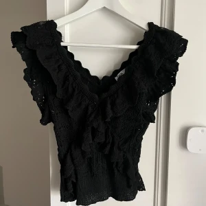 Svart volangtopp med spetsdetaljer - Säljer en svart topp med volanger och spetsdetaljer. Toppen har v-ringning och är ärmlös med breda axelpartier. Köptes på zara för 400kr