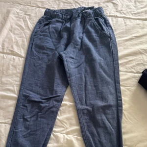 Blå kostymbyxor med resårmidja - Säljer ett par blå kostymbyxor med resår i midjan och sidofickor. Byxorna har en avslappnad passform och är perfekta för chill dagar. Materialet känns mjukt och bekvämt mot huden. Passar till barn 9-10 år.