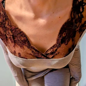 Grå långärmad topp med spetsdetaljer - Säljer en grå långärmad topp med bruna spetsdetaljer och v-ringning. Toppen är figurnära och har en mjuk, stretchig känsla. Perfekt för dig som gillar en feminin touch med spets och vill ha något bekvämt men ändå snyggt.